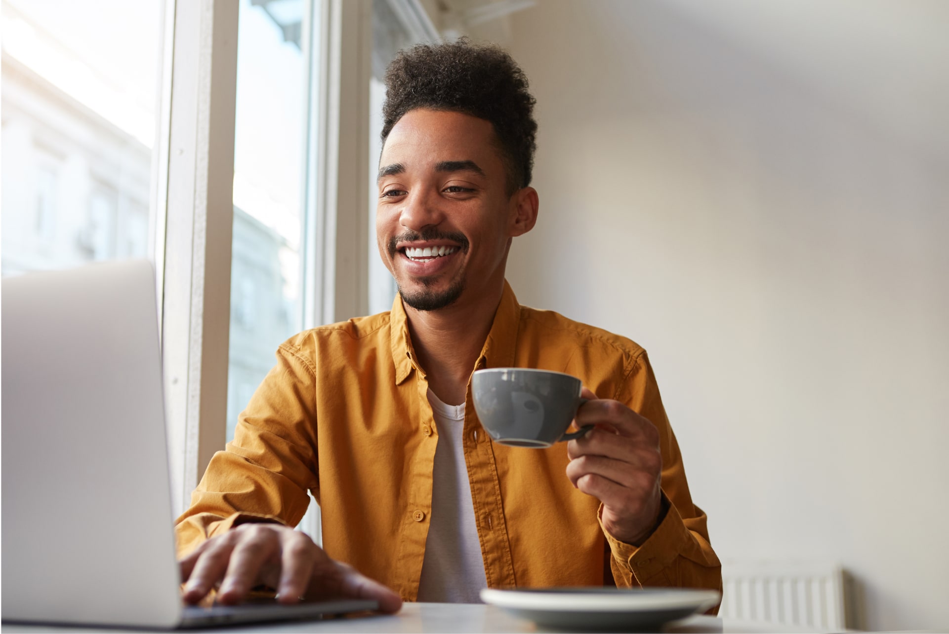 african-american-sitting-table-cafe-working-laptop-wears-yellow-shirt-drinks-aromatic-coffee-communicates-with-his-sister-which-is-far-another-country-enjoys-work 2